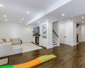 "Open concept basement finishing in Toronto with cozy seating area, fireplace, hardwood flooring, and children's play section