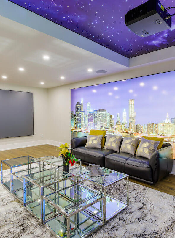 Spacious and modern basement finishing in Toronto with large screen projector, night sky ceiling mural, and cityscape wall art.