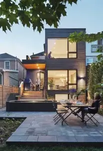 Rear view of a two-storey home addition with dark cladding, large windows and a backyard patio
