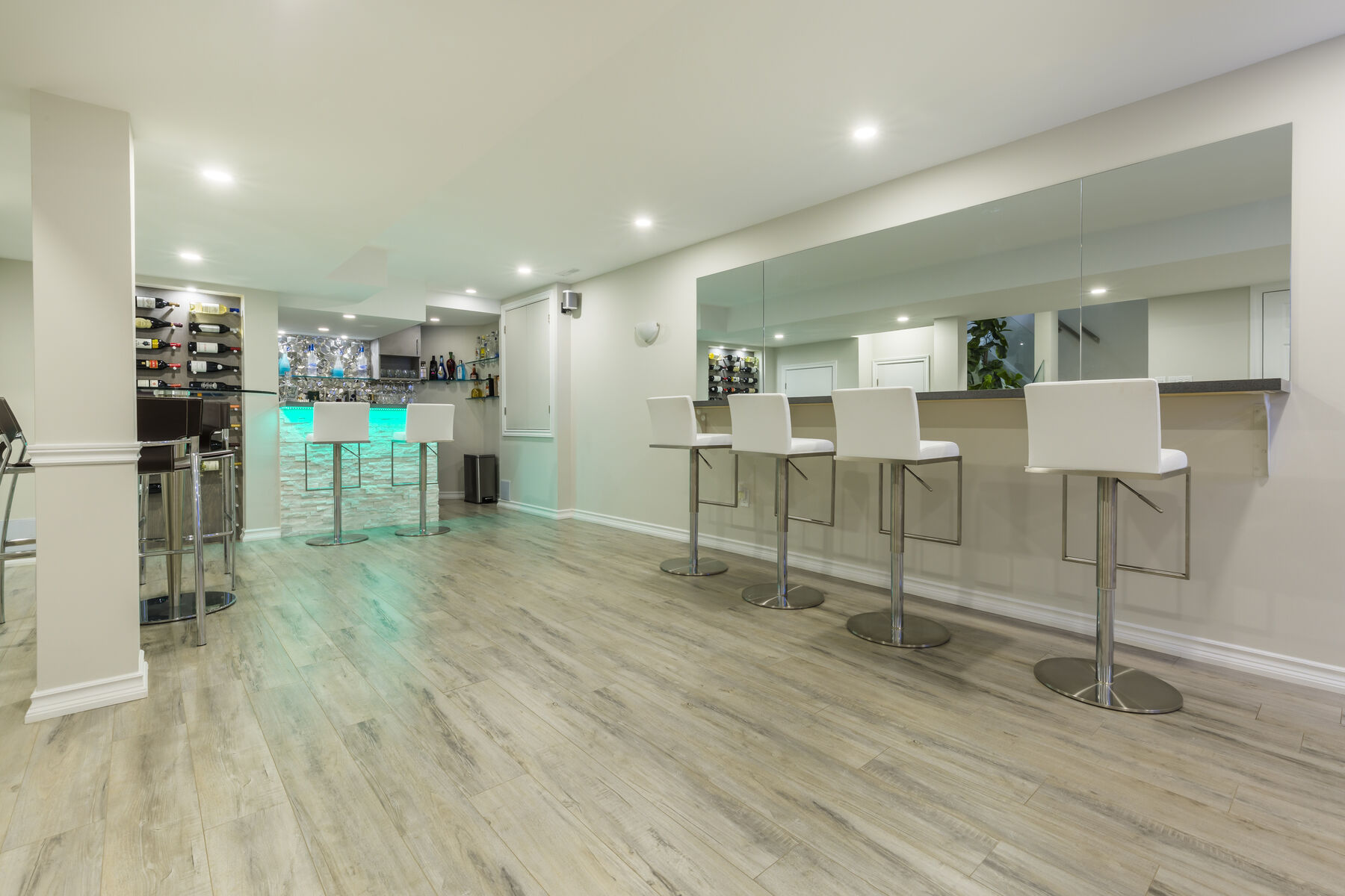 Finished Ajax basement bar with counter seating, a mirrored wall and recessed lighting.
