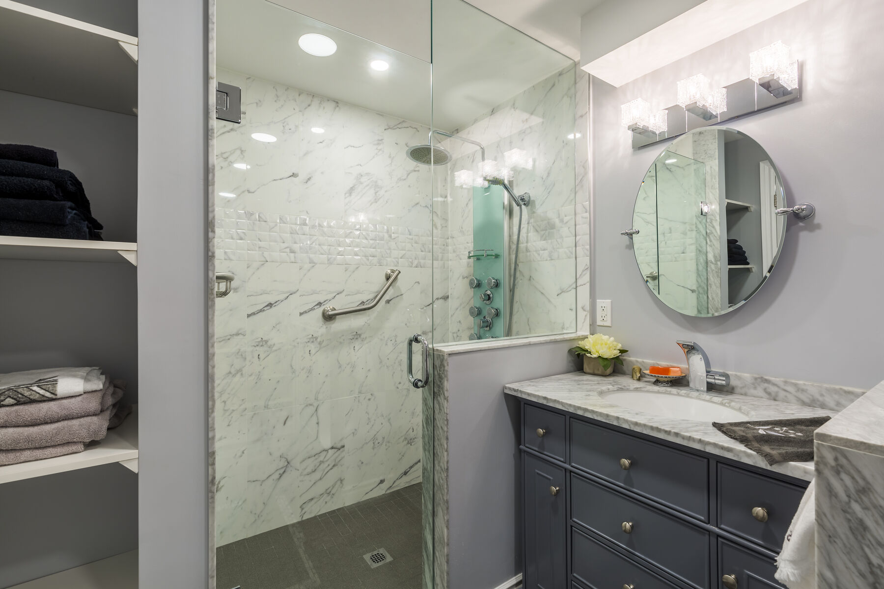 Glass-enclosed shower beside a dark vanity and open towel shelves in a Vaughan bathroom.