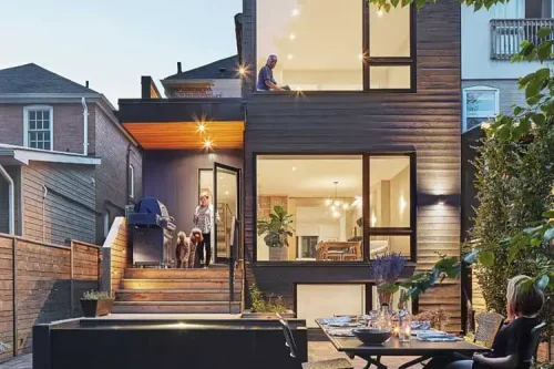 Rear view of a two-storey home addition with dark cladding, large windows and a backyard patio